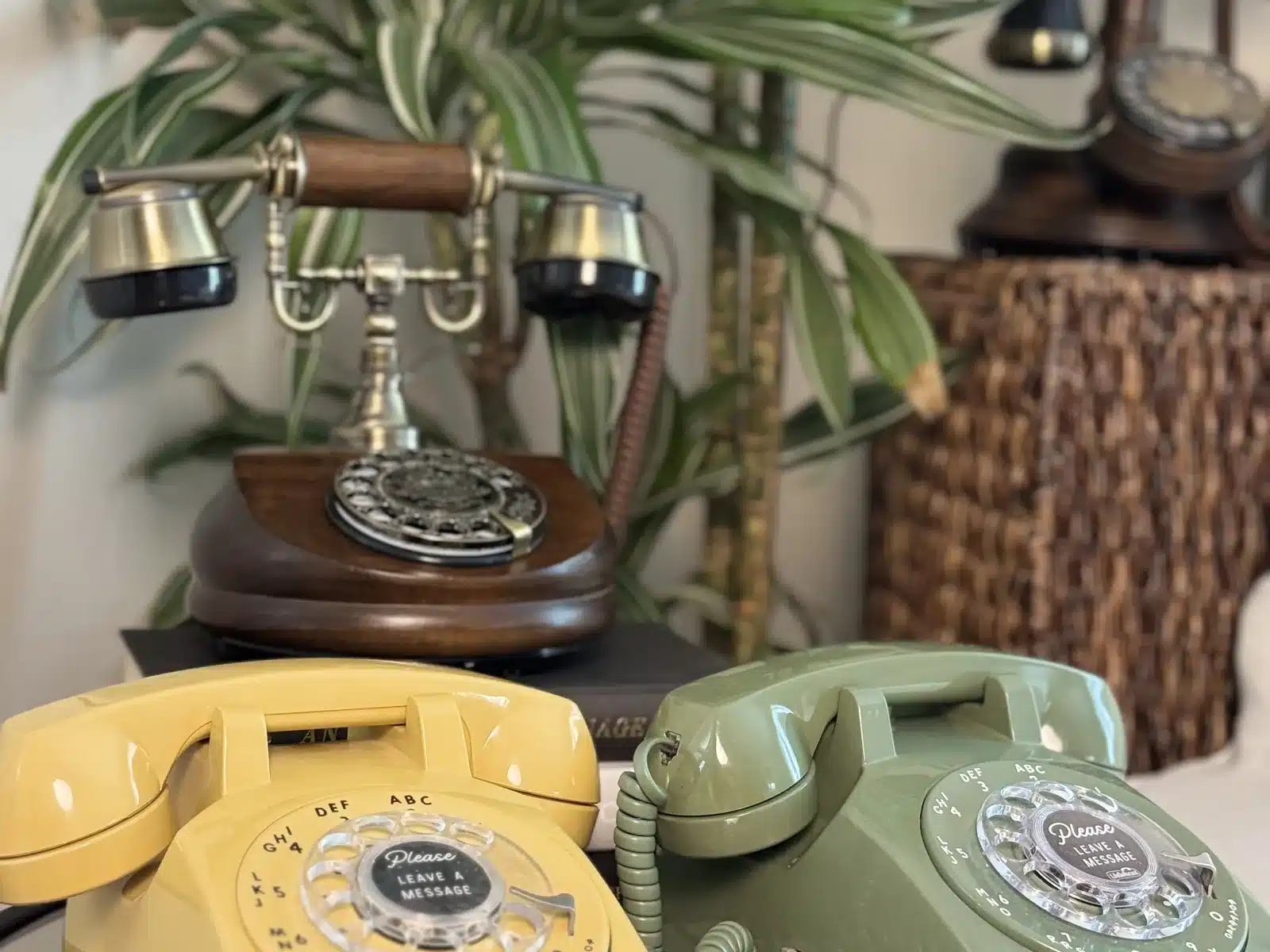 Yellow and sage LifeOnRecord rotary phones arranged beside a wooden antique telephone.