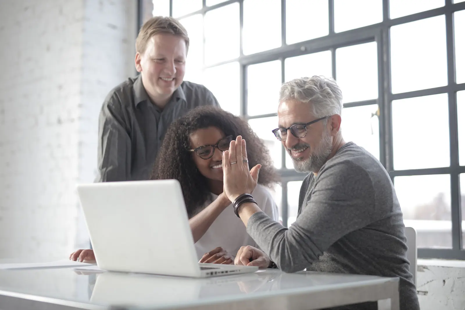 Coworkers of different ages sharing a celebratory high-five around a laptop