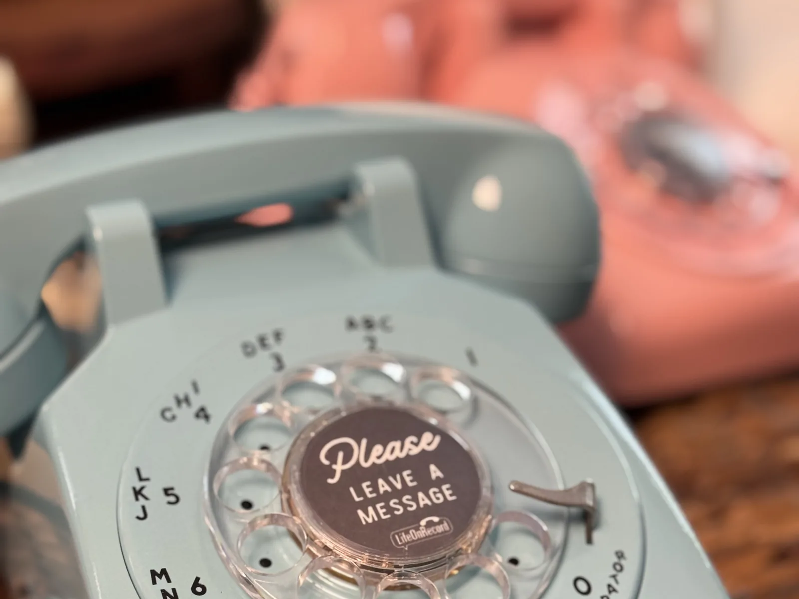 A turquoise LifeOnRecord rotary phone with a coral phone softly in the background.
